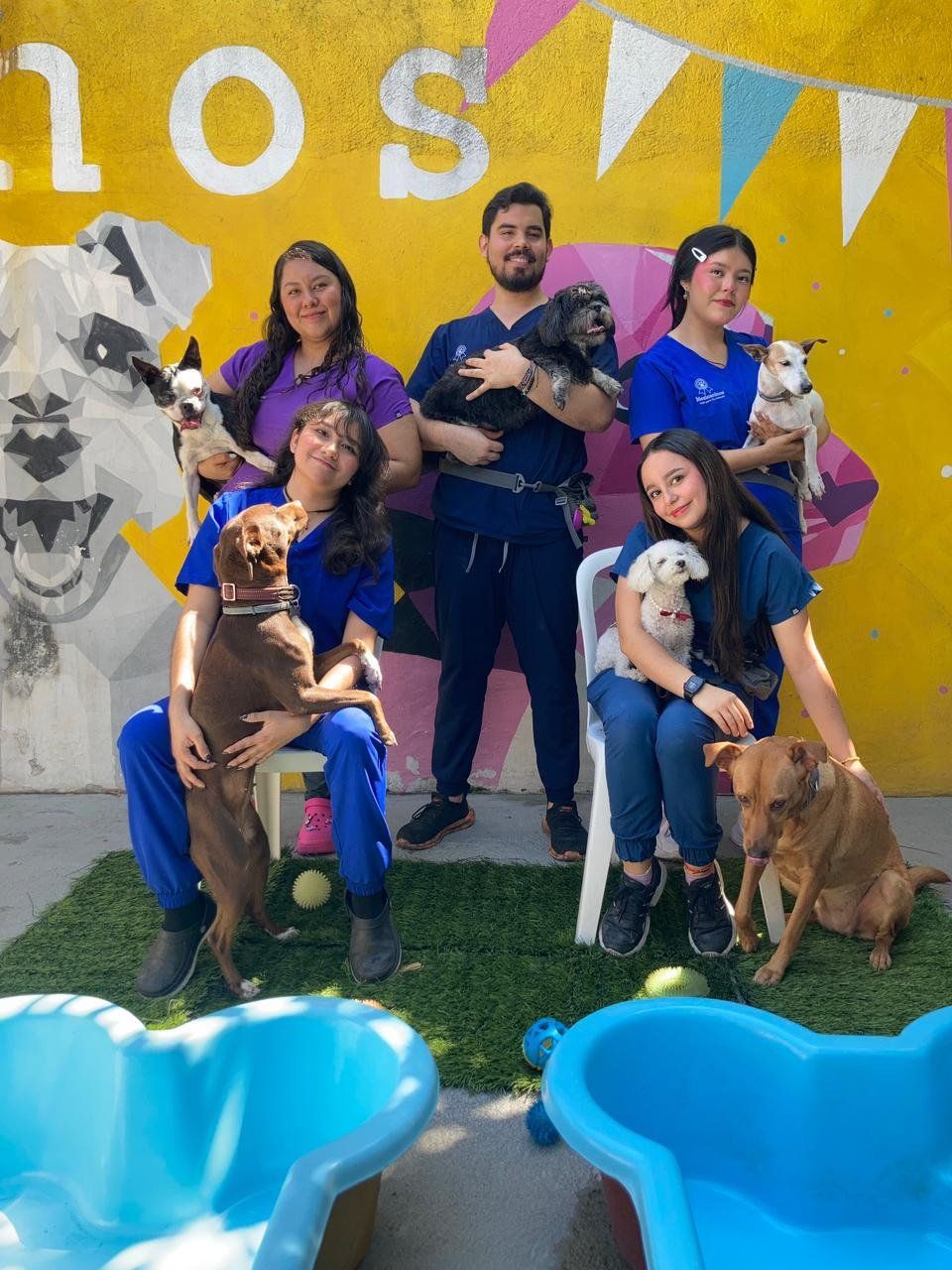 Kenia y el equipo de Mexicaninos con varios perritos frente al mural del patio